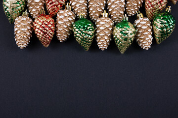 Christmas decorations in the form of red green and gold pine cones with space for text on a black background