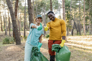 Naklejka na ściany i meble multiracial couple of volunteers cleaning the park from garbage. Walking through the forest and carrying plastic bags. Outdoor cleaning concept.
