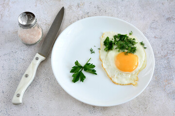 fried egg isolated on white plate with knife and salt shaker, close-up