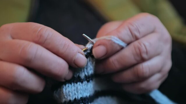 Grandma is knitting a blouse. Close-up of her hands.