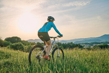 Cyclist Woman riding bike in helmets go in sports outdoors on sunny day a mountain in the forest. Silhouette female at sunset. Fresh air. Health care, authenticity, sense of balance and calmness.