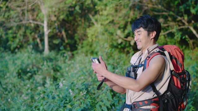 Young asian attractive male tourists takes a photo of a beautiful autumn nature with a view of a lake and a park with his phone and selfie. Walking in the park alone, admiring the beauty nature