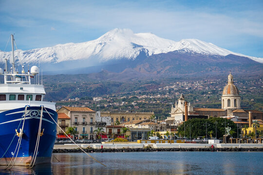 Veduta di riposto dal mare, con il vulcano etna sullo sfondo, le cupole e i campanili delle chiese e una nave in primo piano