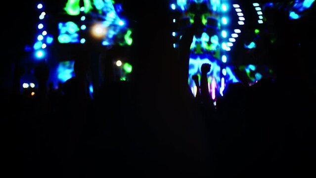 Silhouettes fans raise their hands in front bright colorful strobe lights on stage, Girls in headbands with lights on their heads, people have fun at concert.Crowd is dancing.