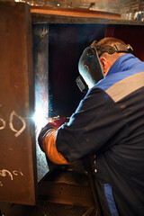 A worker welding metal parts on a construction site. A welder welds parts of a large machine in a...