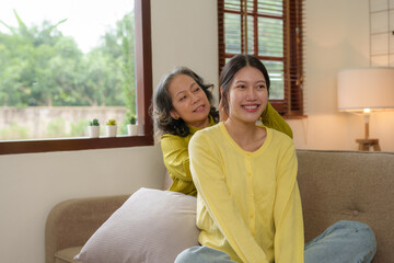 Beautiful Asian woman is taking care of her mother at home in the living room, sitting and resting, having a happy and warm conversation as a mother and daughter.