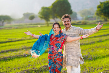 Happy Indian farmer Couple spreading hand and giving expression at agriculture field.