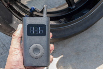 Hand holding a portable inflator is inflating a motorcycle tire.