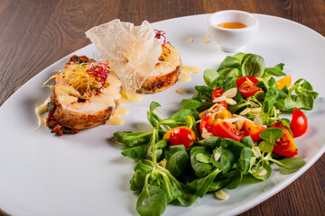 Involtini di pollo servito elegantemente in una braceria con contorno di rucola, pomodori gialli e rossi e scagli di formaggio accompagnati da una salsa agrodolce