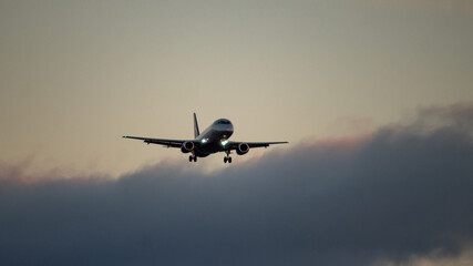 The silhouette of a passenger plane coming in for landing against the backdrop of the sunset sky.