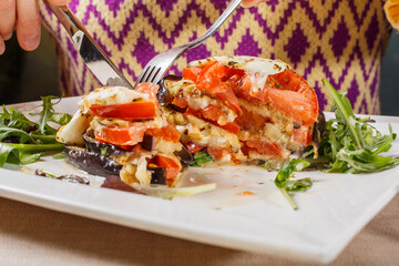 Millefoglie di melanzane con mozzarella filante e pomodori mentre viene tagliata da una cliente in un ristorante elegante
