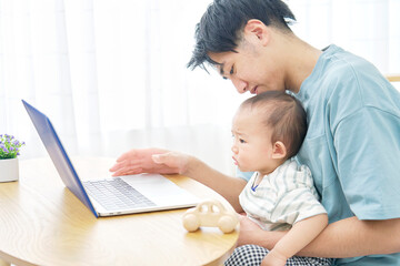 家で赤ちゃんとパソコンを見る父親