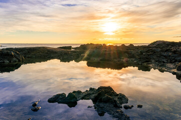 beautiful sea sunrise on a rocky sea coast with calm water , amazing cloudy sky and reflection on water surface