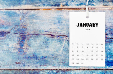The January 2023 calendar page hanged with white rope on old blue wooden background.