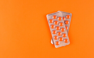 Two blister packs with orange and pills on an orange background