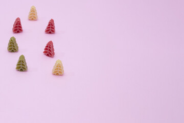 New Year's colorful pasta in the shape of a New Year's tree on a pink background with copy space. New year minimalist scene.