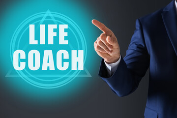 Personal development concept. Businessman pointing at virtual screen with text Life Coach on dark background, closeup
