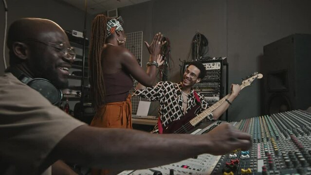 Three cheerful friendly musicians congratulating each other on successful work by high five gesture while recording new music and songs together in studio