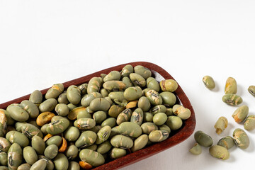 Close-up of dry salted edamame beans, a healthy snack, in a wooden dish on a white background. Copy space.
