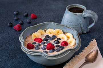 Plant based breakfast of steel cut oats and fruit with coffee on a dark blue surface; copy space