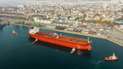 Aerial view of tug boats assisting big oil tanker. Large oil tanker ship enters the port escorted...