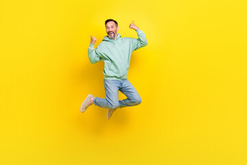 Fototapeta na wymiar Full length photo of confident cool man wear green sweatshirt showing thumbs up jumping high isolated yellow color background