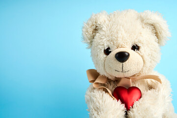 Teddy bear holding heart on blue background with copy space