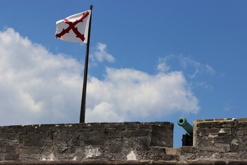 Parapet of a old stone fort flying the Cross of Burgundy with a cannon near by. 