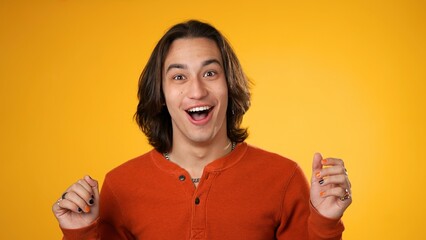 Portrait of amazed gender fluid young man 20s shocked, saying WOW. Handsome guy with long hair surprised isolated on solid yellow background.