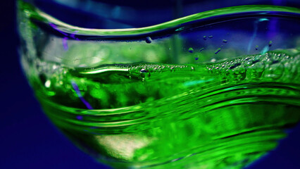 Bartender pours portion of alcohol in the cocktail glass. Stock clip. Making green cocktail at the nightclub isolated on a dark blue wall background.