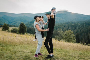 Portrait of happy young family spending time together in field. Mom, dad holds baby son and...