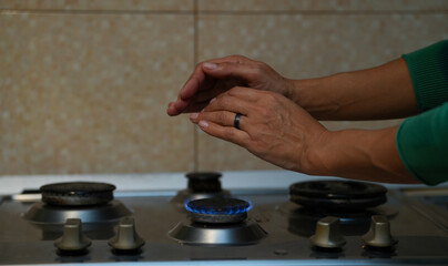 two female hands warming above the stove flame. detail.