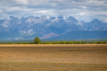 Open fields and majestic mountains in the background. Rural countryside landscape with hills, blue sky with clouds.