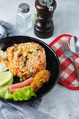 Fried rice with peanuts, carrots, raisins Served with fried chicken, fried egg, and fried sausage. Served on a black plate on a white table in a restaurant.