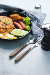 Fried rice with peanuts, carrots, raisins Served with fried chicken, fried egg, and fried sausage. Served on a black plate on a white table in a restaurant.