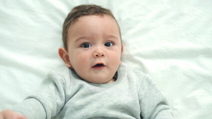 Adorable hispanic baby lying on bed with relaxed expression at bedroom