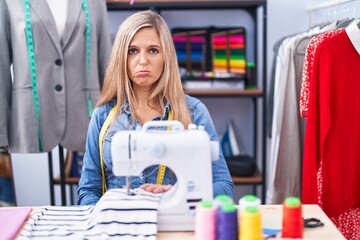 Blonde woman dressmaker designer using sew machine depressed and worry for distress, crying angry and afraid. sad expression.