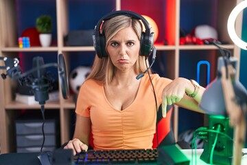 Young woman playing video games pointing down looking sad and upset, indicating direction with fingers, unhappy and depressed.