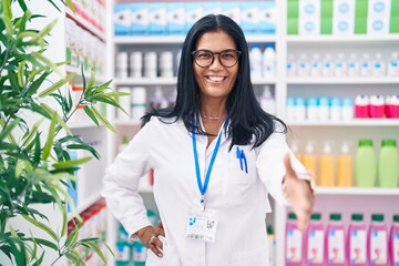 Middle age hispanic woman pharmacist smiling confident shake hand at pharmacy