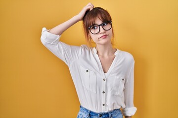 Young beautiful woman wearing casual shirt over yellow background confuse and wondering about...