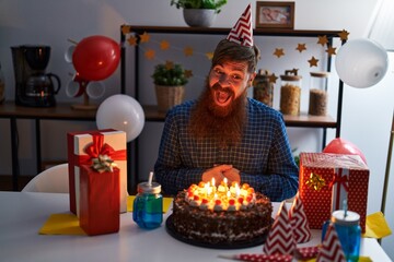 Young redhead man celebrating birthday sitting on table at home