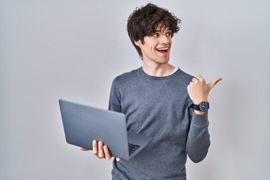 Young man working using computer laptop pointing thumb up to the side smiling happy with open mouth
