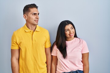 Fototapeta premium Young couple standing over isolated background looking away to side with smile on face, natural expression. laughing confident.