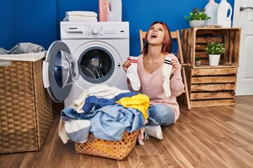 Young caucasian woman doing laundry holding socks angry and mad screaming frustrated and furious, shouting with anger looking up.