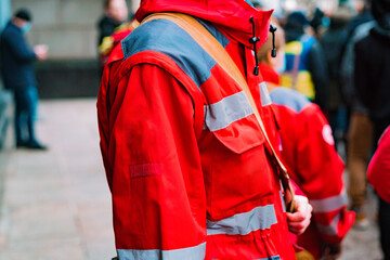 A side view of an emergency medic worker in a red uniform standing on the street during the protest. Ambulance. Assistance. People. Man. Street. Doctor. Paramedic. Urgency. First Aid. Patient. Rescue
