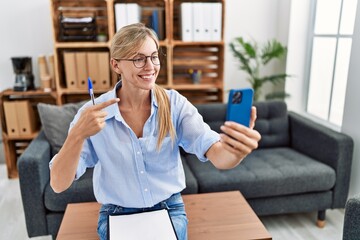 Beautiful woman doing online therapy session at consultation office smiling happy pointing with hand and finger