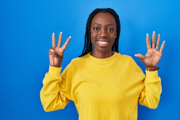 Beautiful black woman standing over blue background showing and pointing up with fingers number eight while smiling confident and happy.