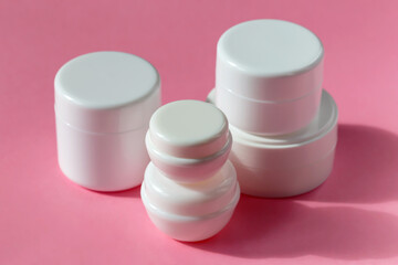Five cosmetic jars on a pink background
