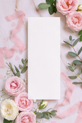 Blank paper card between pink roses and pink silk ribbons on marble top view, wedding mockup