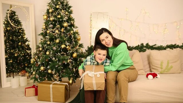 Little boy next to his mother hugging him. Child in the living room gets a Christmas present from his mom and is very happy. Mother and son look very similar